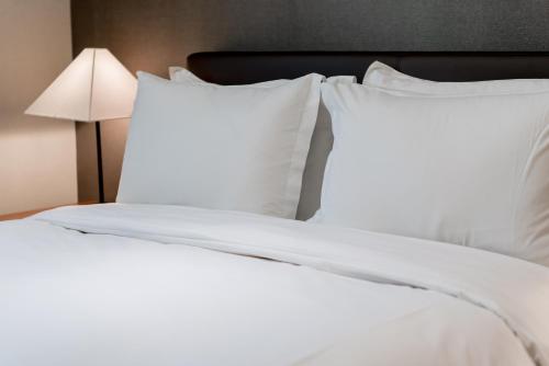 a white bed with white pillows and a lamp at Oriens Hotel & Residences Myeongdong in Seoul