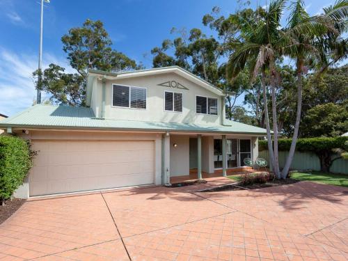 a white house with a garage and palm trees at 8a Foreshore Drive Ducted Air and Boat Parking in Salamander Bay