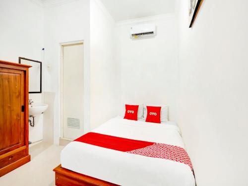 Dormitorio blanco con cama con almohadas rojas en SUPER OYO 3702 Homestay Bougenville Syariah en Lamongan