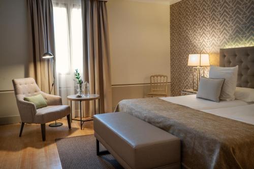 a hotel room with two beds and a chair at Hospes Palacio de Arenales & Spa in Cáceres