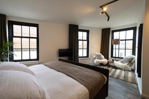 a bedroom with a bed and two chairs and windows at Hotel-restaurant "Lely" in Oude-Tonge