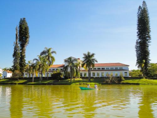 two people in a boat on the water in front of a house at Hotel Metrópole in São Lourenço