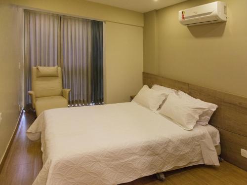 a bedroom with a white bed and a chair at Belíssimo Apartamento Centro de Itaipava All Suites in Itaipava
