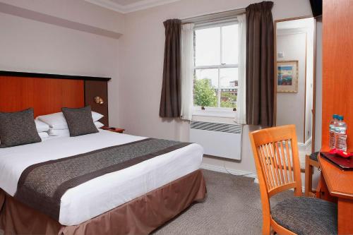 ロンドンにあるベストウエスタン コロナ ホテルのベッド、デスク、窓が備わるホテルルームです。