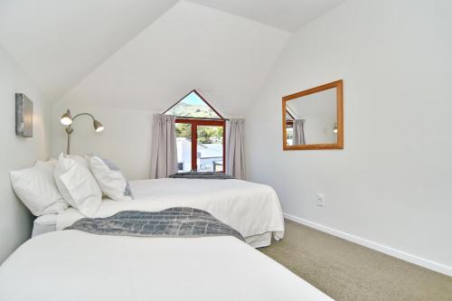 Duas camas num quarto branco com um espelho. em Tumeke Akaroa - Apartment - Christchurch Holiday Homes em Akaroa