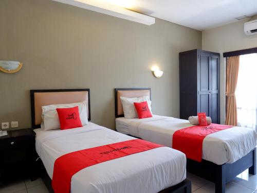 2 bedden in een hotelkamer met rode kussens bij RedDoorz At Jalan Sriwijaya Semarang in Semarang