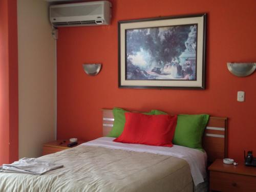 a bedroom with orange walls and a bed with red and green pillows at Libertad Hotel in Trujillo