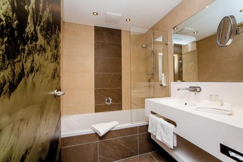 a bathroom with a tub and a sink and a shower at Kaiserhotel Kitzbühler Alpen in Oberndorf in Tirol