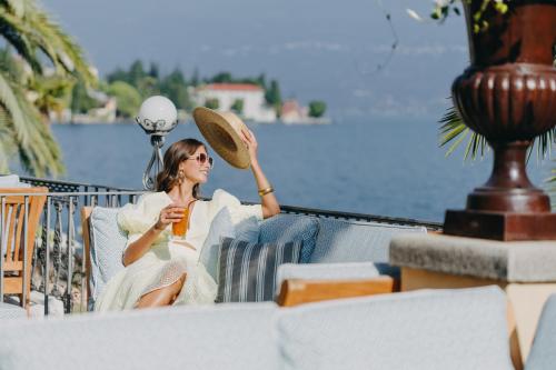 a woman sitting on a balcony with a paddle and a drink at Grand Hotel Fasano in Gardone Riviera