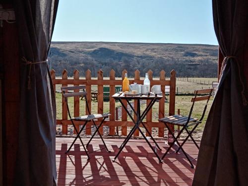 a table and chairs on a deck with a fence at Wee Hoose Glamping Pod 1 in Skail