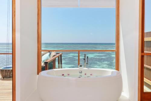 a bath tub in front of a window with the ocean at Kandolhu Maldives in Himandhoo 