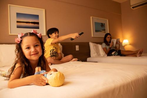 una niña sentada en una cama en una habitación de hotel en Holiday Inn Express Maceió, an IHG Hotel en Maceió