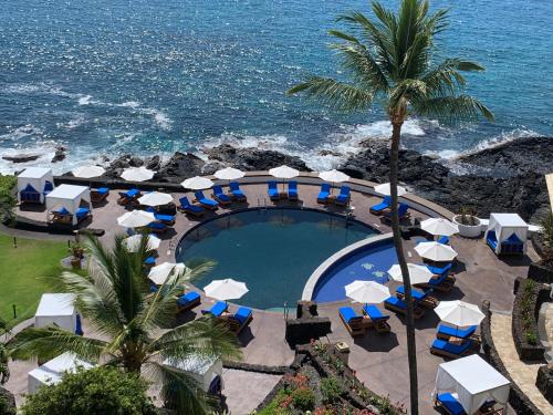 einen Pool mit blauen und weißen Sonnenschirmen und dem Meer in der Unterkunft Royal Kona Resort in Kailua-Kona
