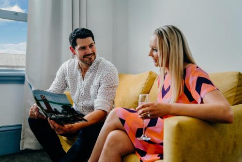 a man and a woman sitting on a couch with a book at The Victoria Hotel Bathurst in Bathurst