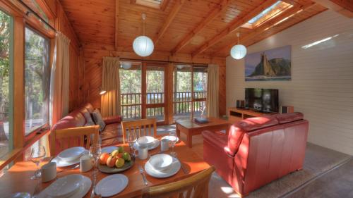 ein Wohnzimmer mit einem Tisch, Stühlen und einem TV in der Unterkunft Stewarts Bay Lodge in Port Arthur