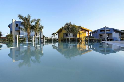 une piscine d'eau avec des maisons et des palmiers dans l'établissement BfB Residence San Marco, à Sciacca