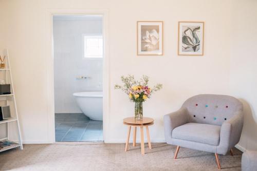 a living room with a chair and a vase of flowers at Tomfoolery Winemaker's Cottage Barossa Valley in Lights Pass