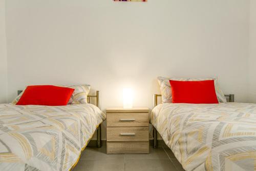 two beds with red pillows and a night stand at 2a Francesca in Vecindario