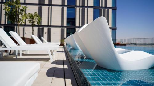 a swimming pool with white chairs on a building at Staybridge Suites Dubai Al-Maktoum Airport by IHG in Dubai