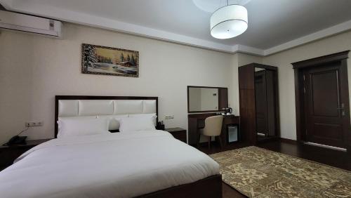 a bedroom with a large white bed and a desk at HOTEL AYNI in Dushanbe