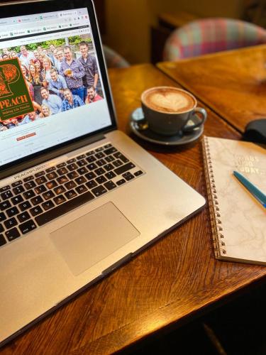 a laptop computer sitting on a wooden table with a cup of coffee at The Richard Onslow in Cranleigh