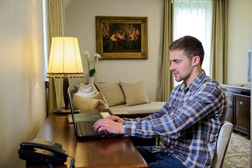 a man sitting at a table using a laptop computer at Hotel & Spa PALIĆ RESORT in Palić
