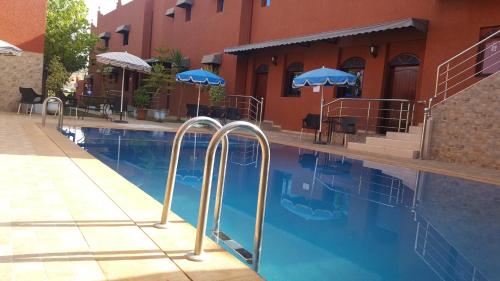 a swimming pool next to a building with blue umbrellas at Hôtel Ajil Cascades D'ouzoud in Ouzoud