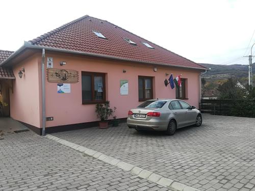 une voiture garée devant un bâtiment rose dans l'établissement Vár-Liget Vendégház, à Kisnána