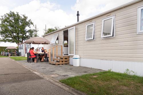 two people sitting at a table outside of a house at Camping De Binnenvaart Superior Chalet in Aan de Wolfsberg