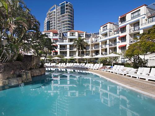 a swimming pool with white chairs and a building at Calypso Plaza Resort Unit 141 in Gold Coast