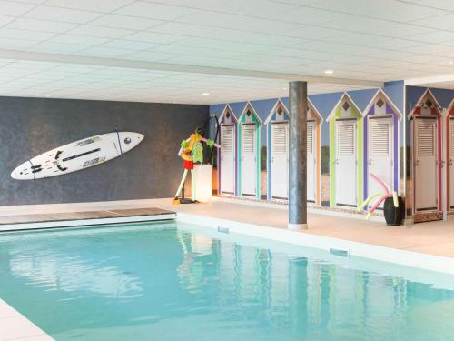 a man standing next to a swimming pool with a surfboard on a wall at ibis Styles Vierzon in Vierzon