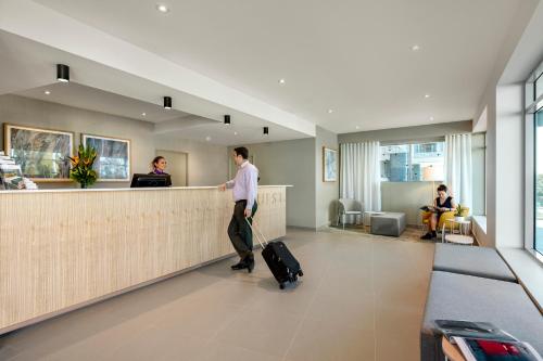 a man with luggage standing at a counter in an airport at Quest Eight Mile Plains in Brisbane