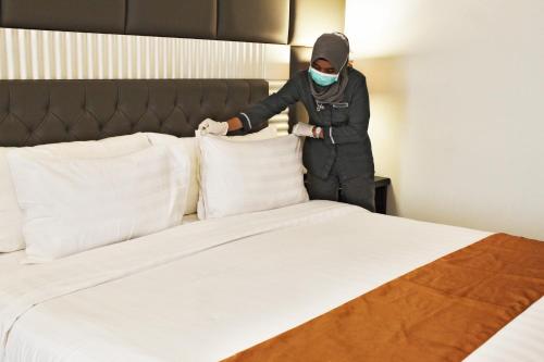 a person in a mask standing next to a bed at Grand Rohan Jogja in Yogyakarta