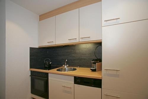 a kitchen with white cabinets and a sink at Apartments Haus Quelle in Leukerbad