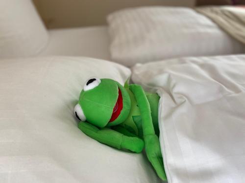 a green stuffed frog laying on a bed at Hotel Wegner - T h e culinary art hotel in Hannover