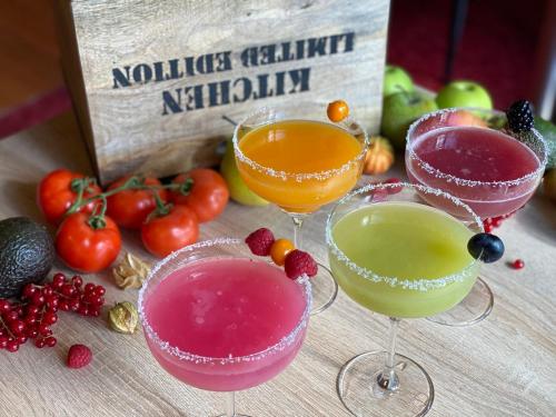 three drinks in wine glasses on a table with fruits and vegetables at Hotel Wegner - T h e culinary art hotel in Hannover