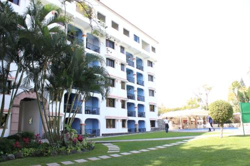 a large white building with a palm tree in front of it at Hotel Coral Cuernavaca Resort & Spa in Temixco
