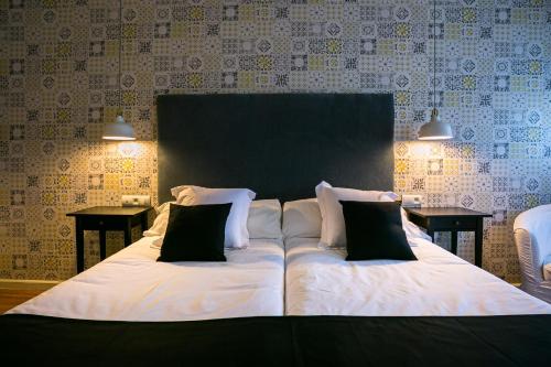 a large bed with white sheets and black pillows at Hotel Spa Sinagoga in Hervás