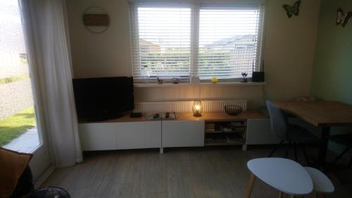 a living room with a television and a desk with a table at Rekerlanden 267 in Warmenhuizen