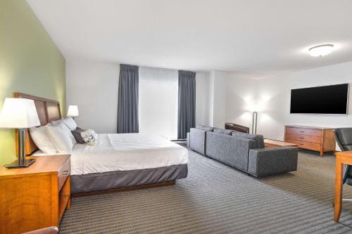 um quarto de hotel com uma cama, um sofá e uma televisão em Hotel Le Victorin, Ascend Hotel Collection em Victoriaville