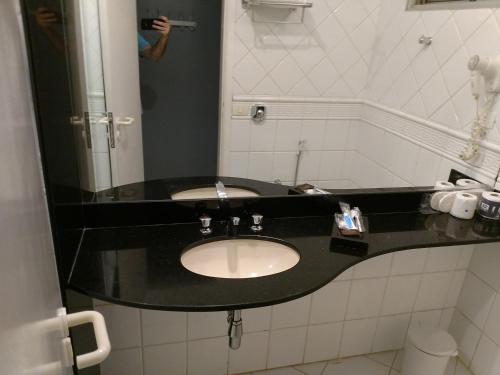 a bathroom with a sink and a person taking a picture at A2 suites - Hotel e Motel in Brasilia