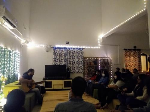 a group of people sitting in a room with a man playing guitar at Hostel Lifespace- Tailor made for working professionals- Luxurious Twin Bungalow with CoWork- only 3 and 4 share Rooms in Pune