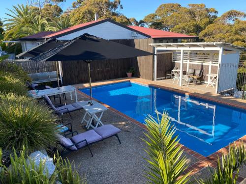 a swimming pool with an umbrella and chairs and a house at Top of the Town Motor Inn in Narooma