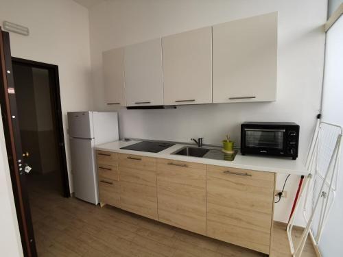 una cucina con armadi bianchi, lavandino e forno a microonde di All' Ombra del Faro - Mini Apartments a Taranto