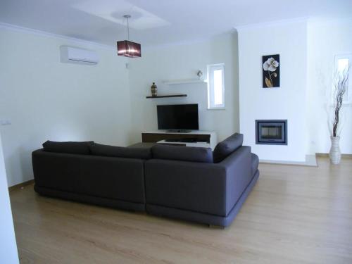 a living room with a black couch and a television at Casa São Bartolomeu - 5 Quartos com Piscina in São Bartolomeu
