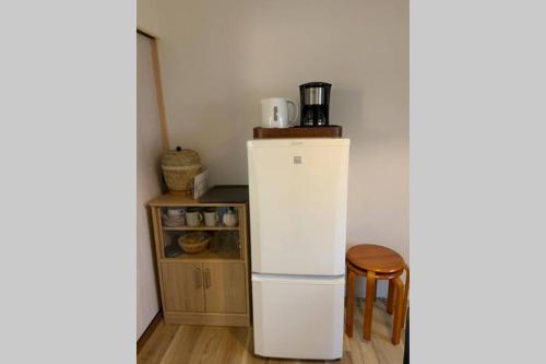 a small kitchen with a white refrigerator and a stool at Kyoto Osaka SUMIREYA in Takatuki
