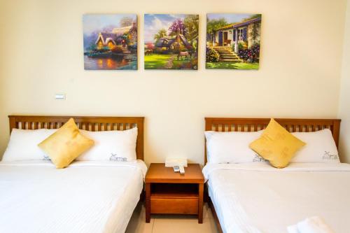 two beds in a room with paintings on the wall at Kenting Muchen INN in Hengchun