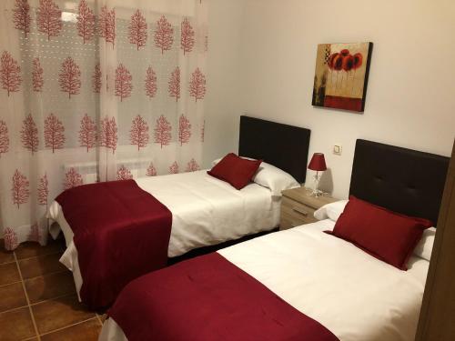 Habitación con 2 camas y sábanas rojas y blancas. en Alojamientos El Chorro, en Los Navalucillos