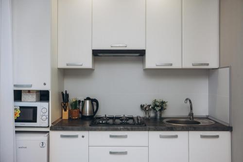 a kitchen with white cabinets and a sink and a microwave at Apart-hotel I. Sirko New Building 7 floor in Sumy