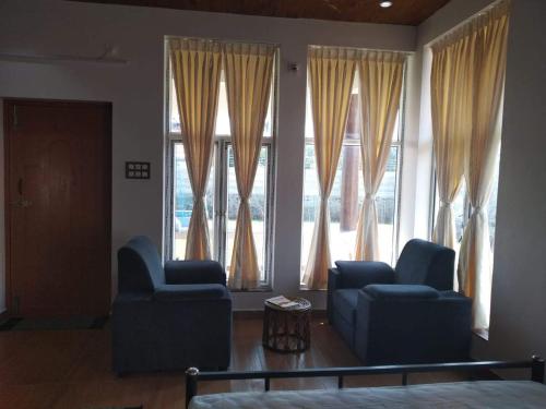 a living room with two blue chairs and large windows at Waves Beach House in Puducherry